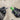 A close-up of two gloved hands holding a Greenlee battery charger and a metal screwdriver against a blurred concrete background.