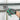 Hand wearing a black glove holding green metal cutting pliers under a metal shelf.
