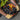 Close-up of a person wearing work gloves reaching into a black open-top tool bag with orange lining and trim. The bag is filled with screwdrivers, pliers and other hand tools, with additional tools and accessories stored in the exterior pockets.