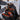 Person wearing orange and black gloves opening a tool backpack filled with tools in a workshop setting.