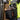 A close-up of a black work utility belt worn by a person in a high-visibility vest. The belt has multiple pockets, orange trim, and is shown holding yellow-handled pliers.